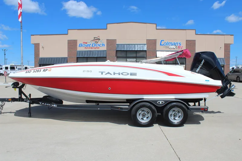 The Image of 2022 Tahoe 2150 boat on trailer, displayed outside dealership under clear blue sky. - 0