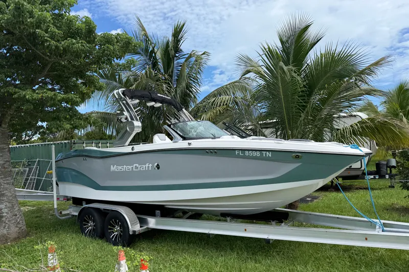 The Image of 2023 MasterCraft X24 boat on trailer, surrounded by palm trees. - 0