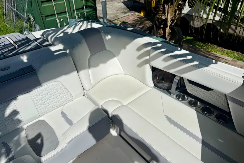 Slide: The Image of 2023 MasterCraft X24 boat interior with white seating and cup holders, shaded by palm leaves. - 10