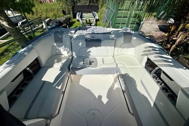 Slide: The Image of 2023 MasterCraft X24 boat interior with white seating and cup holders, surrounded by greenery. - 6