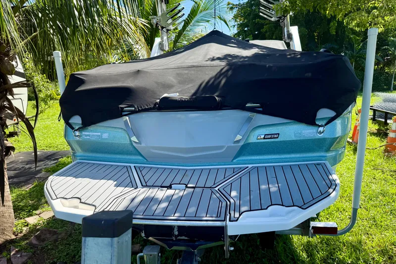 Slide: The Image of 2023 MasterCraft X24 boat with cover, parked outdoors, surrounded by lush greenery. - 9