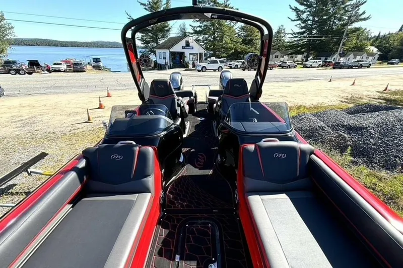 Slide: The Image of 2022 Manitou XT 27 SRW pontoon boat interior with red and black seating, near a lakeside. - 28