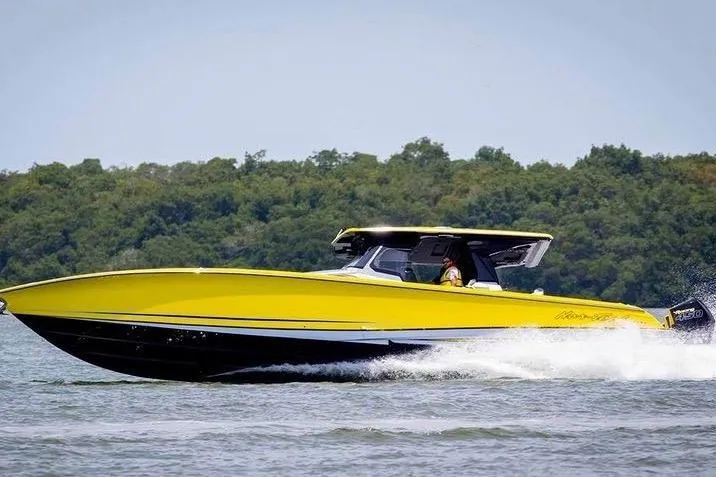 Slide: The Image of 2021 Nor-Tech 450 Sport boat in vibrant yellow, cruising on a lake with lush green trees. - 2