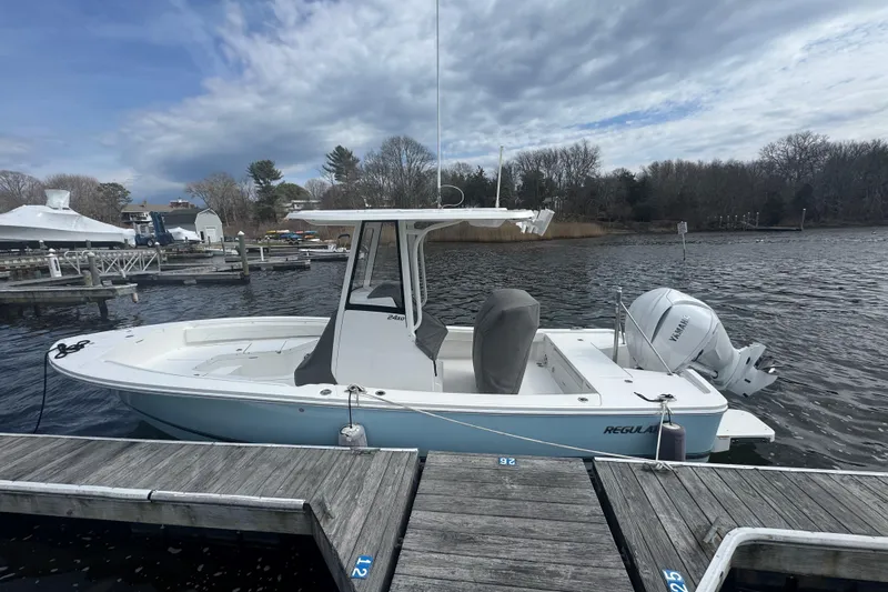 Slide: The Image of 2021 Regulator 24XO boat docked by a serene waterfront under a cloudy sky. - 2
