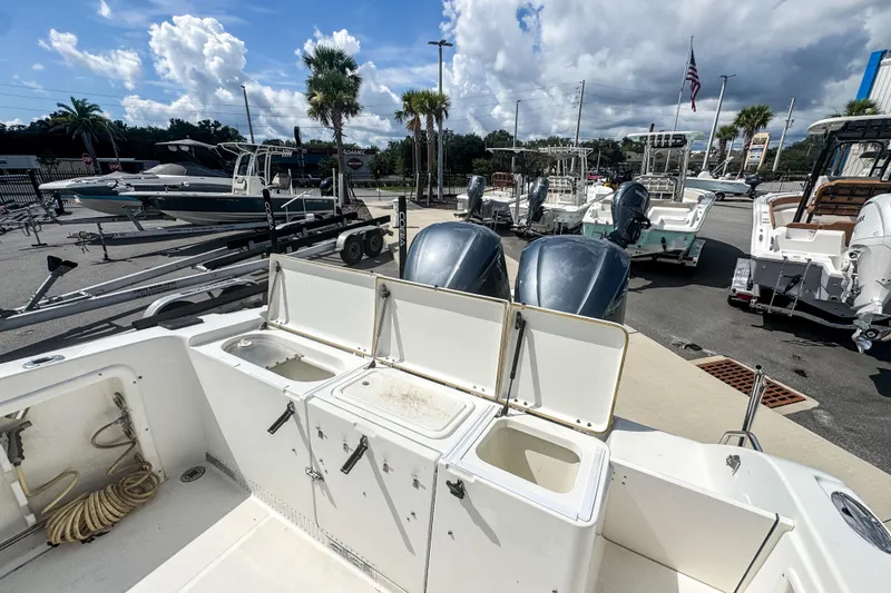 Slide: The Image of 2003 Triton 2895 CC boat with open compartments, parked among other boats under a cloudy sky. - 13
