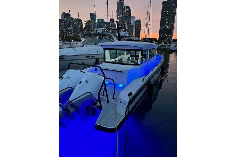 Slide: The Image of 2024 Axopar 37 XC Cross Cabin Wet Bar with blue LED lights at sunset marina. - 18