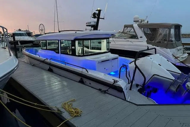 Slide: The Image of 2024 Axopar 37 XC Cross Cabin Wet Bar docked, illuminated with blue lights at dusk. - 19