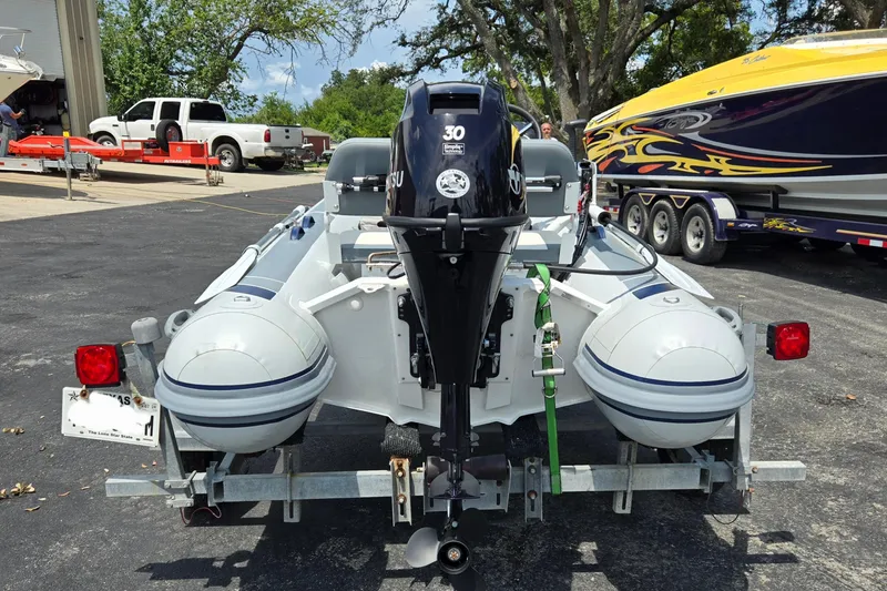 Slide: The Image of 2025 Highfield Classic 360 inflatable boat on trailer, parked near colorful speedboat. - 5