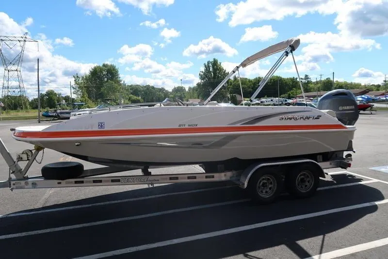 Slide: The Image of 2020 Starcraft MDX OB 211 E OB boat on trailer, parked outdoors under a cloudy sky. - 4