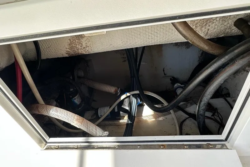 Slide: The Image of 2007 Edgewater 245CC boat interior showing wiring and hoses in storage compartment. - 23