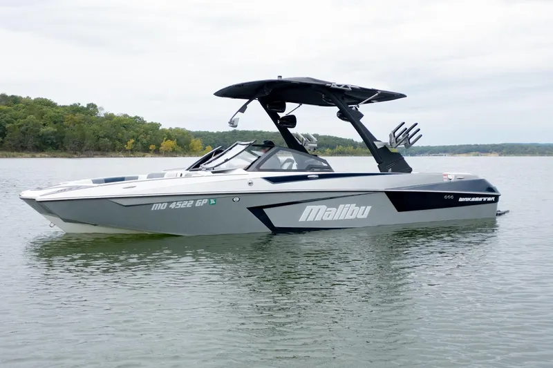 Slide: The Image of 2021 Malibu Wakesetter 23 MXZ boat on a calm lake with forested shoreline. - 2