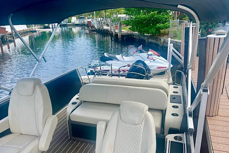 Slide: The Image of 2022 Premier Solaris 230 pontoon boat docked by waterfront homes, featuring beige seating. - 9