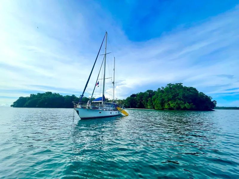 Slide: The Image of Sailboat Aleutian 51 (1977) anchored near lush island under blue sky. - 30