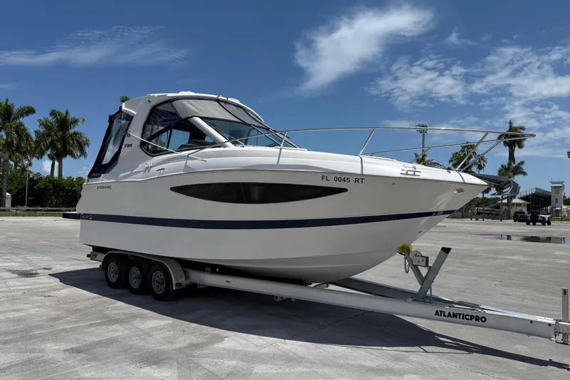 The Image of 2012 Four Winns V305 boat on trailer, parked outdoors under a clear blue sky. - 1