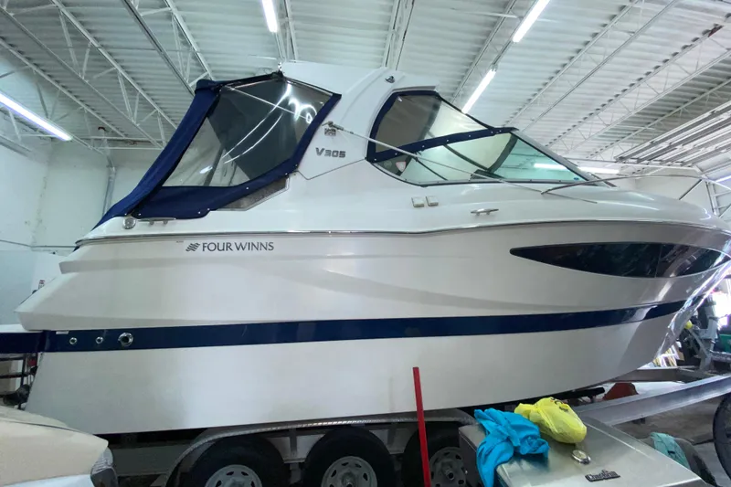 Slide: The Image of 2012 Four Winns V305 boat in indoor storage, side view with blue accents. - 11