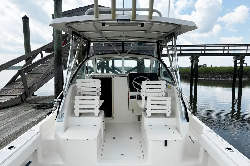Slide: The Image of 2005 Pursuit 2870 Walkaround boat docked, featuring helm and seating area under a clear sky. - 10