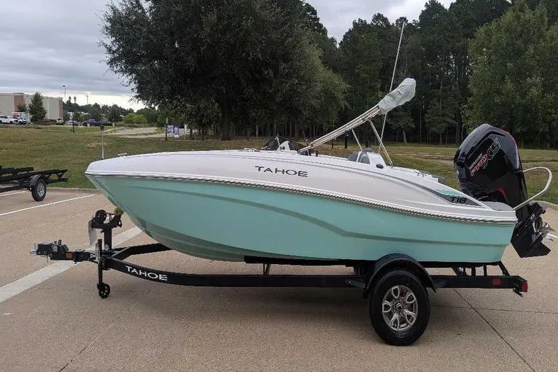 Slide: The Image of 2026 Tahoe T18 boat on trailer, parked outdoors, with trees in the background. - 2