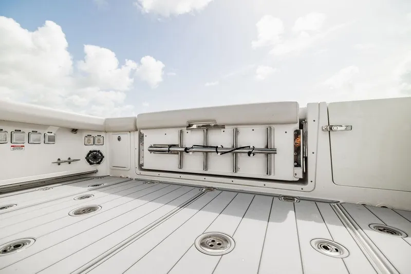 Slide: The Image of 2019 Boston Whaler 380 Realm deck with storage compartments and rod holders under a cloudy sky. - 10