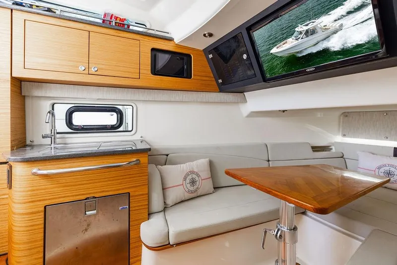 Slide: The Image of 2019 Boston Whaler 380 Realm interior with kitchenette, seating, and TV displaying boat image. - 32
