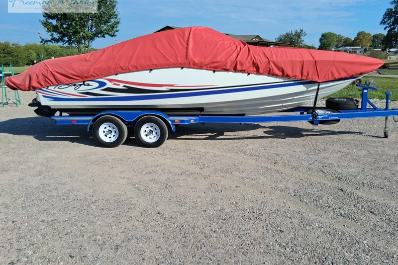 Slide: The Image of 2007 Baja 245 boat with red cover on blue trailer, parked on gravel. - 15