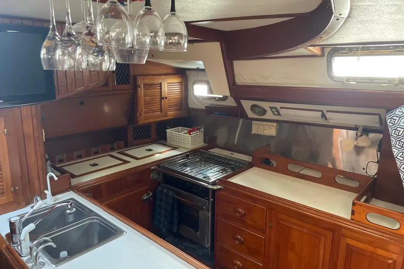 Slide: The Image of 1981 Mariner 48 yacht kitchen with wooden cabinetry, stove, sink, and hanging glassware. - 19