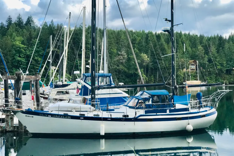 Slide: The Image of 1981 Mariner 48 sailboat docked in a serene marina with forest backdrop. - 46