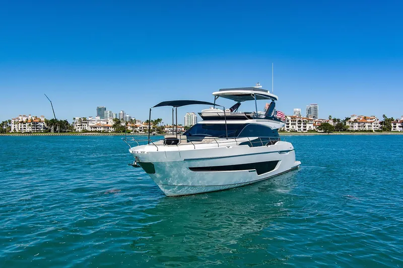 Slide: The Image of 2021 Fairline Squadron 68 yacht cruising on clear blue waters near a coastal cityscape. - 2