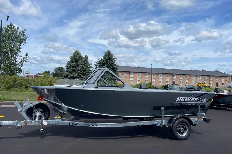 Slide: The Image of 2026 Hewescraft 180 Sportsman boat on trailer, parked outdoors under a cloudy sky. - 2