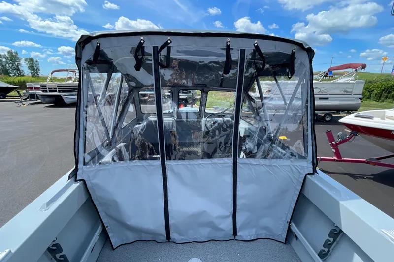 Slide: The Image of 2026 Hewescraft 180 Sportsman boat with clear canopy, parked outdoors under blue sky. - 6