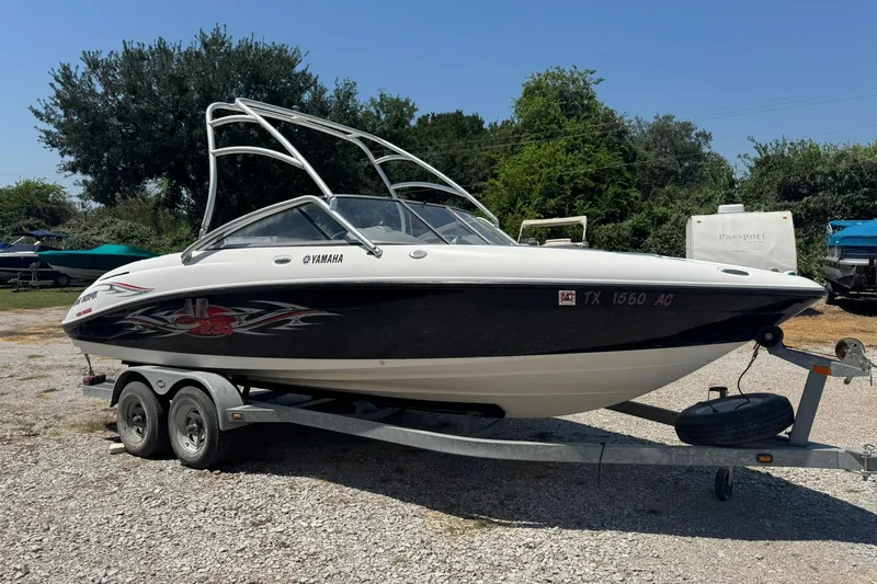 Slide: The Image of 2006 Yamaha Boats AR230 HO on trailer, parked outdoors, surrounded by trees and other boats. - 2