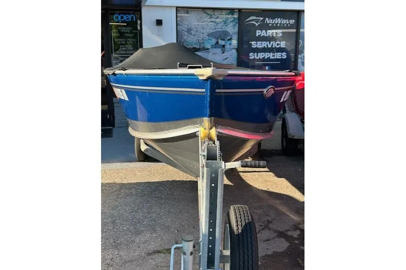Slide: The Image of 2023 Lund 1600 Fury SS boat on trailer, parked outside marine supply store. - 2
