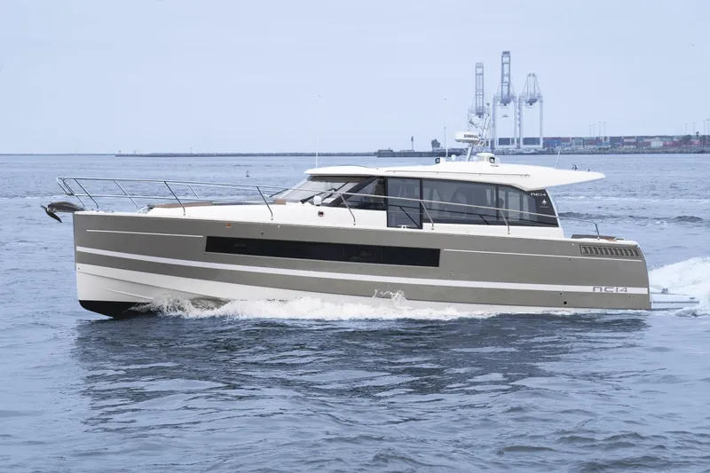 Slide: The Image of 2014 Jeanneau NC 14 yacht cruising on open water near industrial port. - 2