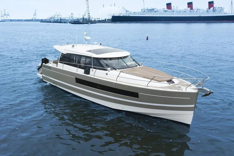 Slide: The Image of 2014 Jeanneau NC 14 yacht cruising in a harbor with a large ship in the background. - 3