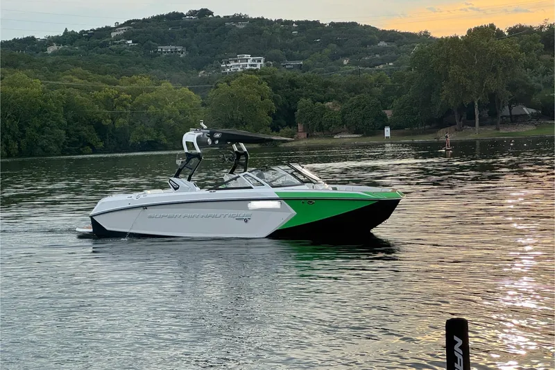 Slide: The Image of 2017 Nautique Super Air Nautique G23 boat on a serene lake with lush green hills. - 2