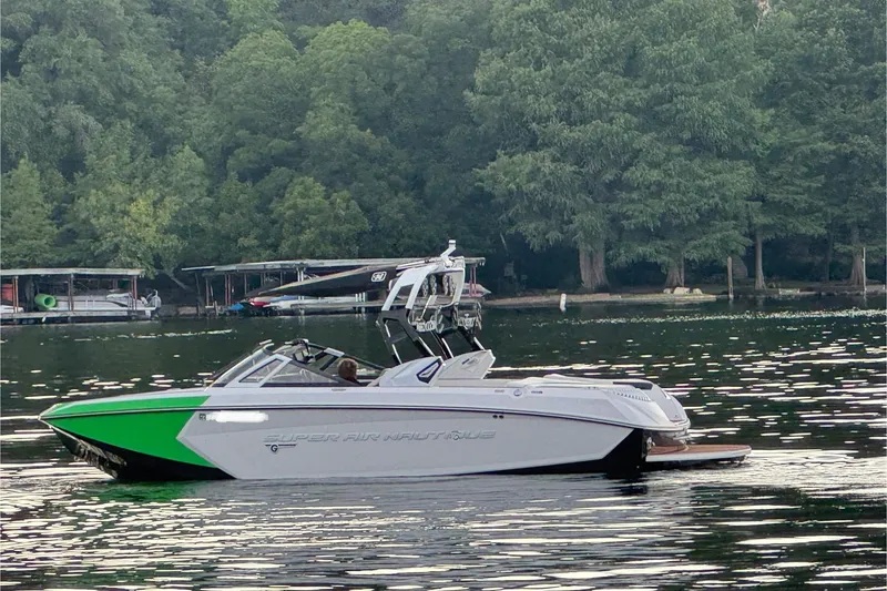 Slide: The Image of 2017 Nautique Super Air Nautique G23 boat on a serene lake with lush trees. - 4