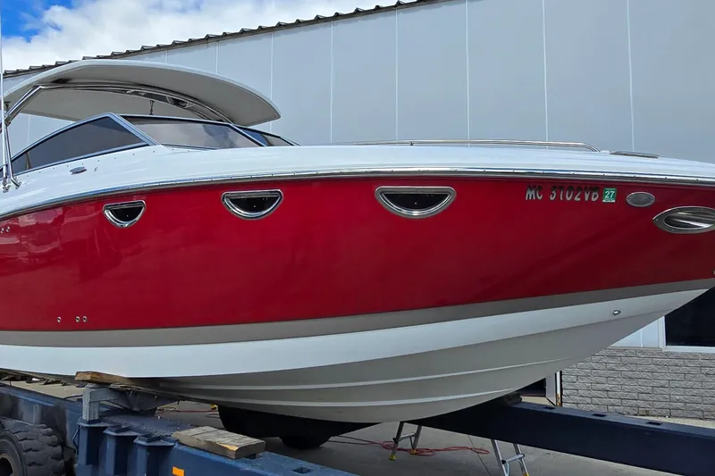 The Image of 2011 Cobalt 323 boat with red hull on trailer, parked near a building. - 1