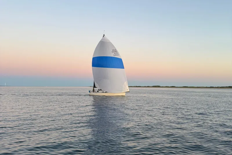 Slide: The Image of Sailboat J/122 from 2013 on calm waters at sunset, featuring a blue and white spinnaker. - 55