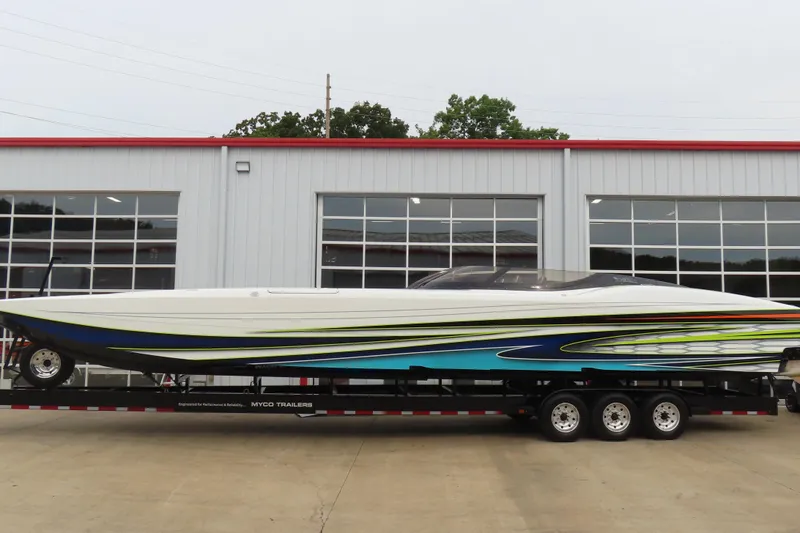 The Image of 2022 MTI 48 boat on trailer, vibrant design, parked outside industrial building. - 0