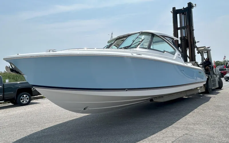 Slide: The Image of 2026 Pursuit DC 326 boat on forklift, light blue hull, parked outdoors. - 2