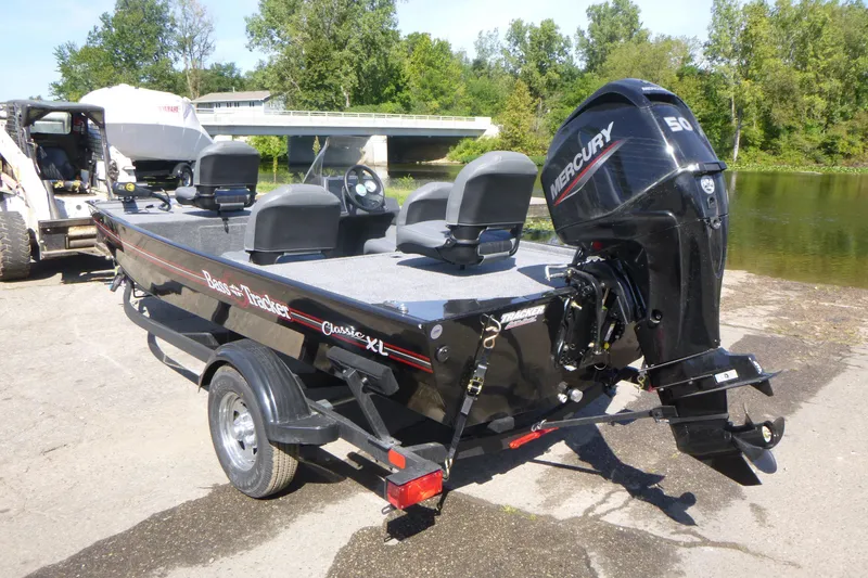 Slide: The Image of 2026 Tracker Bass Tracker Classic XL boat with Mercury engine, parked near a river. - 3