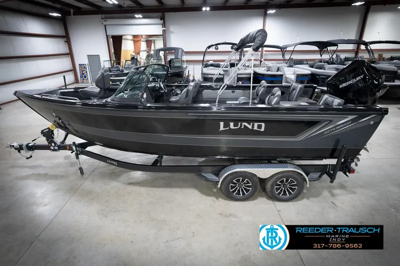 The Image of 2026 Lund 2275 Baron boat in showroom, side view, on trailer, with Mercury engine. - 2