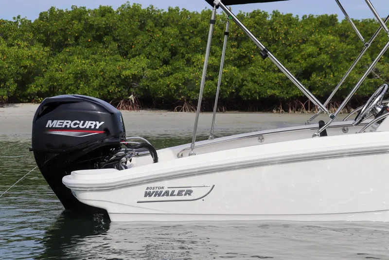 Slide: The Image of 2026 Boston Whaler 130 Super Sport boat with Mercury engine near lush shoreline. - 12