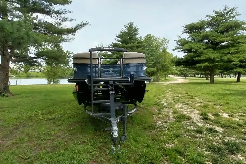 Slide: The Image of 2022 Regency 250 DL3 pontoon boat on trailer, surrounded by lush greenery. - 10