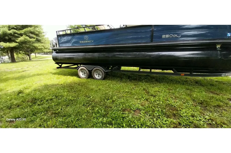 Slide: The Image of 2022 Regency 250 DL3 pontoon boat on trailer, parked on grassy area. - 13