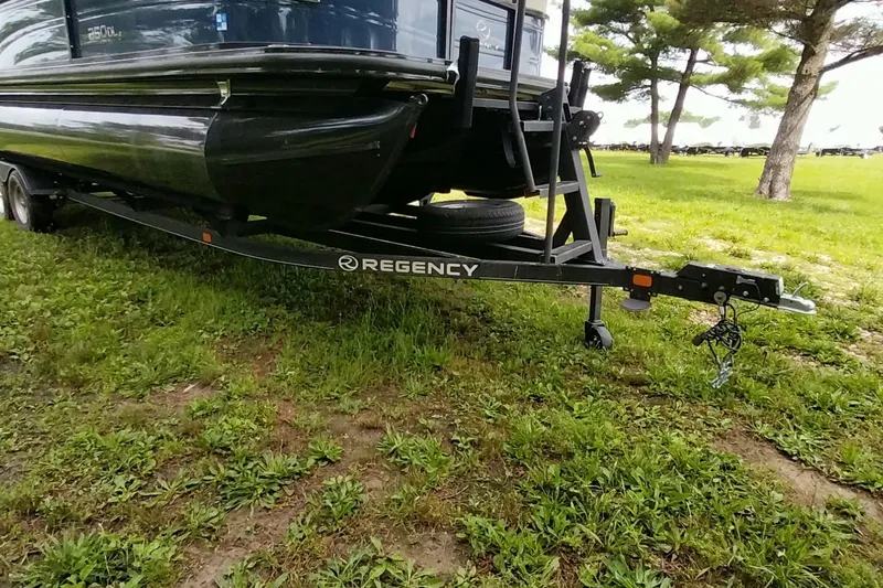 Slide: The Image of 2022 Regency 250 DL3 boat on trailer, parked on grassy area with trees. - 14