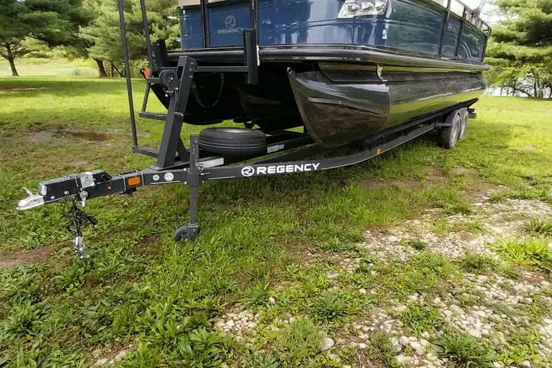 Slide: The Image of 2022 Regency 250 DL3 pontoon boat on trailer, parked on grassy area. - 15