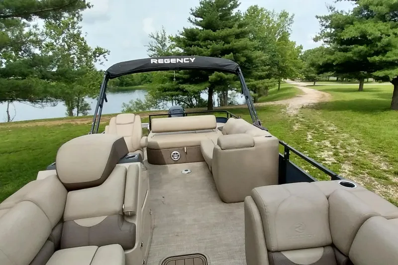 Slide: The Image of 2022 Regency 250 DL3 pontoon boat with beige seating, near a scenic lake and trees. - 4