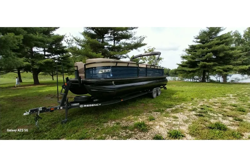 Slide: The Image of 2022 Regency 250 DL3 pontoon boat on trailer, parked on grassy area near trees. - 9