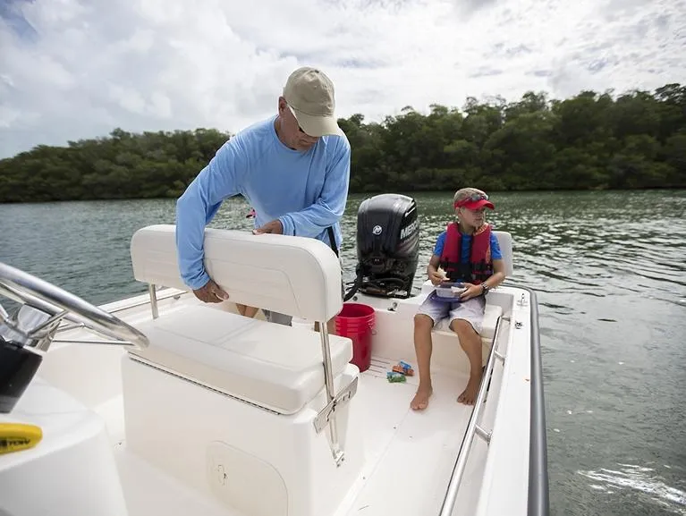 Slide: The Image of 2026 Boston Whaler 170 Montauk boat interior with seating and motor, docked by a serene waterway. - 10