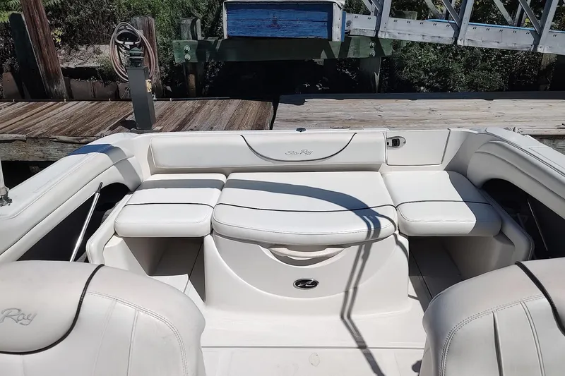 Slide: The Image of 2004 Sea Ray 215 Weekender boat interior with white seating and dock background. - 14